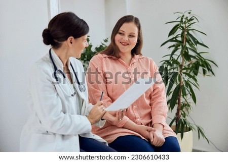 A satisfied female nutritionist holding a paper with weight loss progress and smiling with an overweight female patient.