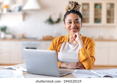 Satisfied good looking young African American stylish woman, freelancer, student or real estate agent, sitting at her desk at home office, looking at the camera and smiling pleasantly