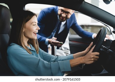 Satisfied happy caucasian female client customer woman sitting at the wheel of new car doing test-drive before buying auto while male shop assistant helping her choose it - Powered by Shutterstock