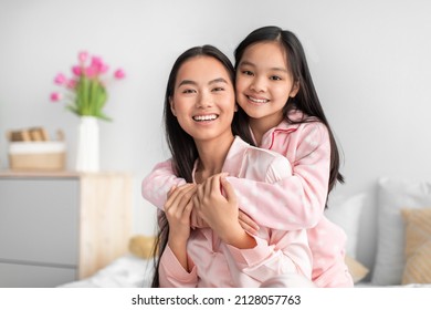 Satisfied Happy Cute Teen Girl Hugging Young Japanese Woman In Pajama Celebrating Mother's Day In Bedroom. Mom And Daughter Enjoy Good Morning Together At Home During Covid-19 Quarantine, Copy Space