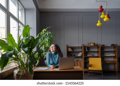 Satisfied happy female employee relaxing at workplace in modern office, sitting in chair in front of laptop, receiving good news. Businesswoman enjoying break during workday. Happiness at work concept