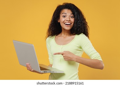 Satisfied Happy Smiling Jubilant Cheerful African American Young Brunette Woman 20s Wears Green Shirt Hold Use Work On Laptop Pc Computer Pointing On It Isolated On Yellow Background Studio Portrait