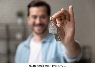 Satisfied Homeowner. Blurred Portrait Of Happy Young Man Buyer Renter Of New Modern Home Apartment Holding Key Demonstrating Wellbeing Wealth Celebrate Achievement. Focus On Hand With Keys Of Dwelling