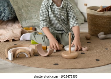 Un niño satisfecho e interesado se sienta en una habitación infantil de estilo escandinavo y recoge una pirámide ecológica de madera en una alfombra redonda Vestida con una camisa y unos pantalones verdes