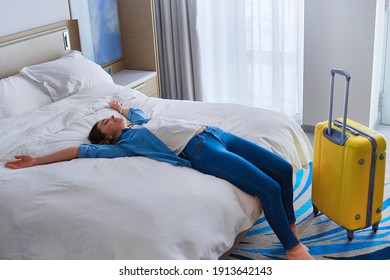 Satisfied joyful traveler woman lying on a bed in hotel bedroom after check-in and rejoicing travel start. Enjoy holiday and vacation. Happy moment