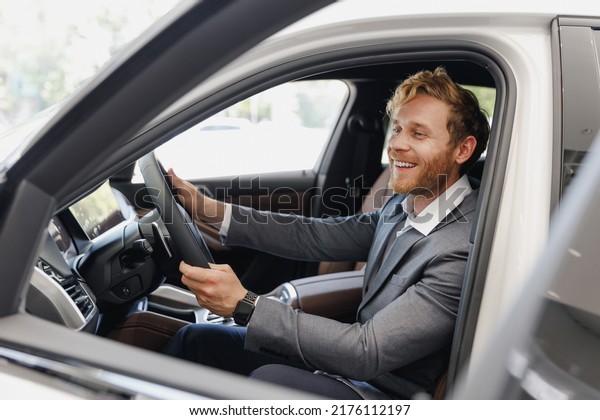 Satisfied man customer male buyer client wear\
classic grey suit driving car hold wheel choose auto want buy new\
automobile in showroom vehicle salon dealership store motor show\
indoor Sale concept.