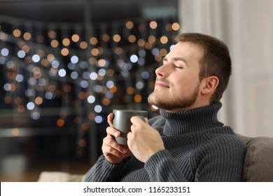 Satisfied Man Enjoying Smelling A Coffee Mug Sitting On A Couch In The Living Room At Home In The Night