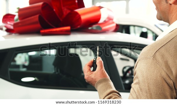 A satisfied man looks at his new car and shows the key\
to it