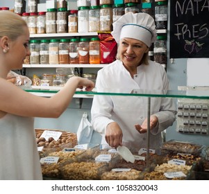 Satisfied Mature Woman Offering Client Different Nuts In Local Supermarket