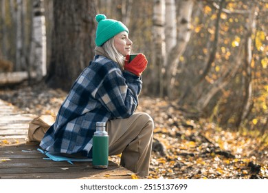 Satisfied middle aged woman spending tranquility time alone walking in autumn forest dreaming drinking hot thermos tea. Relaxed pleased female rest on eco path enjoys calm late fall park, stress free. - Powered by Shutterstock