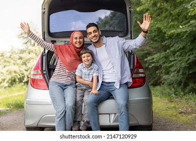 Satisfied Millennial Arab Husband, Wife In Hijab And Small Boy Waving Hands Sitting In Car Trunk, Outdoors In Summer, Free Space. Family Weekend, Vacation Together And Auto Trip And Life Insurance