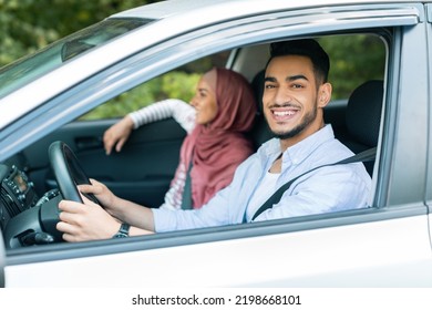 Satisfied Millennial Arab Male Driving At Steering Wheel, Looks At Camera, Rides With His Wife In Hijab In Car And Enjoys Journey At Summer. Road Travel Together, Love Relationship And Family Vacation