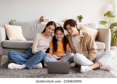 Satisfied Millennial Japanese Mom, Dad And Teen Daughter Sitting On Floor And Watching Video On Laptop In Living Room Interior. Modern Technology, Chat, Blog, Video Call At Home And Social Distance