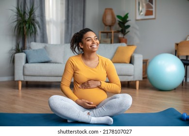 Satisfied millennial pregnant african american lady touching big belly feels movement of baby, practicing yoga, look at free space in living room interior. Health care, sports at home and motherhood - Powered by Shutterstock