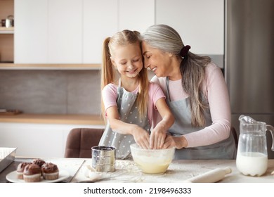 Satisfied Old Female In Apron Hugs Little Granddaughter, Make Dough, Have Fun In Minimalist Kitchen Interior, Free Space. Hobby At Spare Time Together, Cooking Lesson Baking And Prepare Food Home