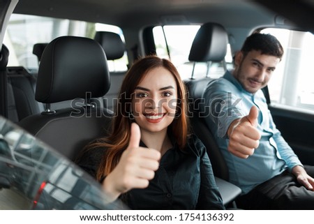 Satisfied with the purchase of a new car, a young couple shows a thumbs up while sitting in a car inside