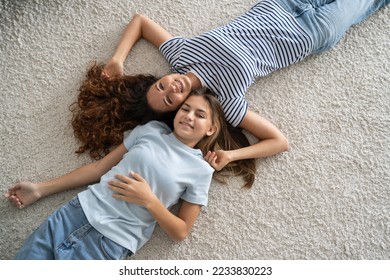 Satisfied relaxed woman nanny and teen girl both lie on floor in apartment and smiled look at camera top view. Happy close-knit family life of mother and daughter of school age dressed in casual style - Shutterstock ID 2233830223