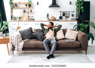 Satisfied Relaxed Young Indian Man Chilling On Sofa In Living Room, Smiling. Handsome Arabian Guy Have Rest At Home, After Laptop Distant Work, Dreaming About Vacations, Throwing His Hands Behind