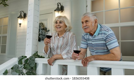 Satisfied senior elderly caucasian couple drinking wine in porch at home. Happy mature retired family of grandfather and grandmother looking ahead, enjoying life together - Powered by Shutterstock