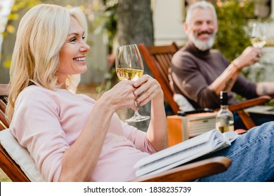 Satisfied senior woman holding a glass of wine talking with her grey-haired husband in the garden