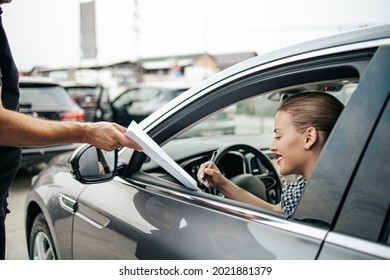 Satisfied And Smiled Female Buyer Sitting In Her New Car. She Happy While Signing Buyer's Purchase Contract With Used Car Seller.