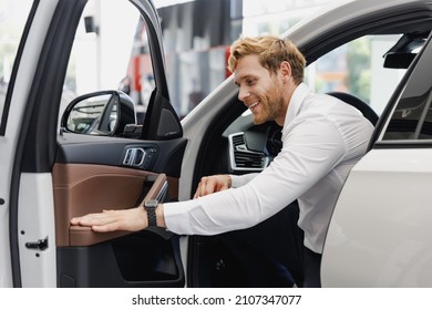 Satisfied smiling happy man customer male buyer client in white shirt get out car salon drive chooses auto wants buy new automobile in showroom vehicle dealership store motor show indoor Sales concept