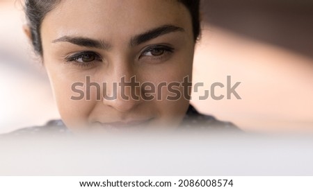 Satisfied smiling Indian employee working at computer banner close up face portrait. Young millennial business woman sitting at monitor, looking at display, watching, reading content