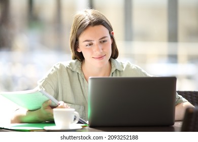 Satisfied student e learning with laptop and notes in a coffee shop