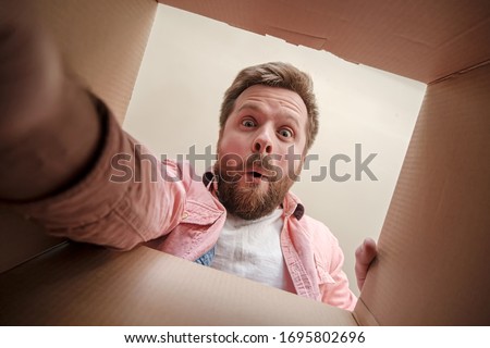 Satisfied, surprised man holds out his hand, trying to get a gift or parcel from an unpacked box. Unboxing inside view.