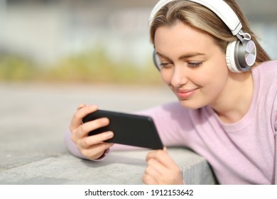 Satisfied teen watching media on smart phone sitting in a park