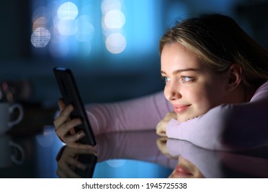 Satisfied Teen Watching Smart Phone Content On A Table In The Night At Home