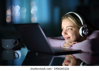Satisfied teen wearing headphones watching media on laptop in the night at home