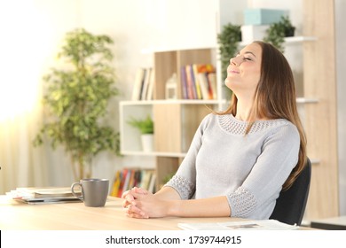 Satisfied Woman Breathing Fresh Air Sitting On A Desk In The Living Room At Home