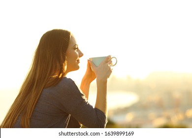 Satisfied woman contemplating sunset holding coffee mug from a balcony