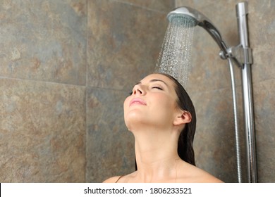 Satisfied woman having shower relaxing with water falling on head on a bathroom