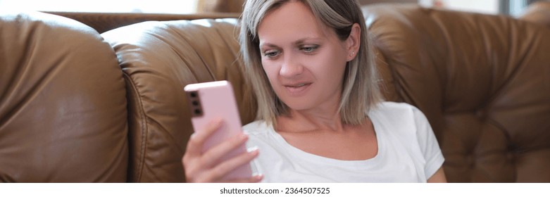 Satisfied woman holding smartphone and looking at screen while sitting on couch. Buying and chatting online concept. - Shutterstock ID 2364507525