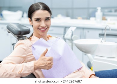 Satisfied woman patient showing her perfect smile and gesturing thumb up after treatment, sitting in dentist clinic - Powered by Shutterstock