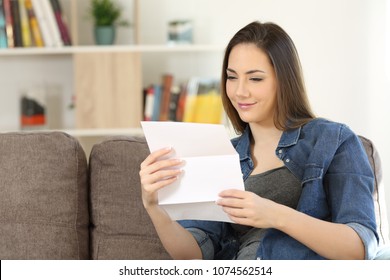 Satisfied woman reading a letter sitting on a couch in the living room at home
