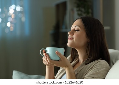 satisfied woman relaxing smelling coffee in the night sitting on a couch in the living room at home - Shutterstock ID 1822641020