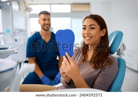 Satisfied woman using mirror while checking her teeth after appointment at dentist's office.