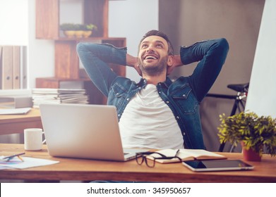 Satisfied with work done. Happy young man working on laptop while sitting at his working place in office - Shutterstock ID 345950657