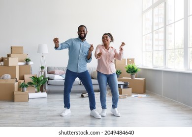 Satisfied Young Afro American Couple Dancing In Flat With Cardboard Boxes In Home Interior, Free Space. Man And Woman Enjoying New Apartment Together, Happy Buying House. Credit, Relocation And Rental