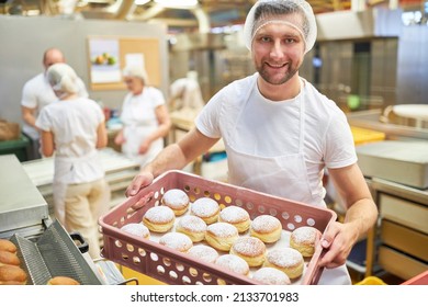 Satisfied young man as a baker apprentice carries fresh Berlin pancakes in the bakery - Powered by Shutterstock