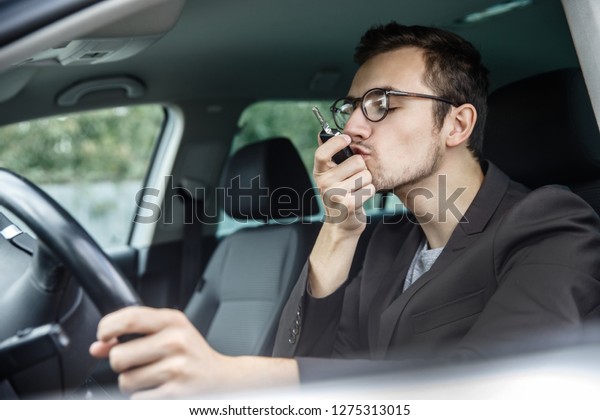 Satisfied young man\
is kissing his car keys while sitting at the car. His left hand is\
on the steering\
wheel.