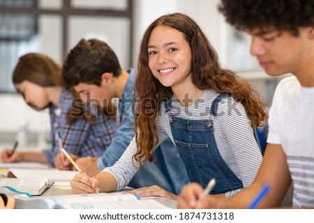 Satisfied young woman looking at camera. Team of multiethnic students preparing for university exam. Portrait of girl with freckles sitting in a row with her classmates during high school exam.