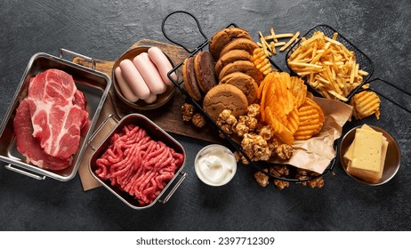 Saturated and trans. Unhealthy food. Sausage, potato, meat, cheese, popcorn, cookies, cream on dark background. Top view.