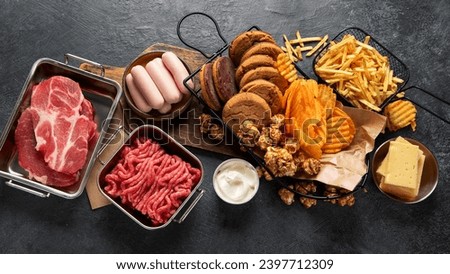 Saturated and trans. Unhealthy food. Sausage, potato, meat, cheese, popcorn, cookies, cream on dark background. Top view.