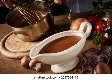 Sauce boat filled with rich brown spicy gravy viewed high angle on a kitchen table with assorted fresh vegetable ingredients