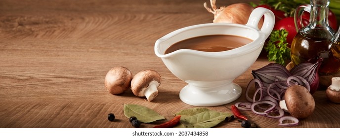 Sauce boat or sauciere filled with a rich brown gravy surrounded by fresh vegetable ingredients on a wood background with copyspace in panorama banner format