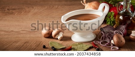 Sauce boat or sauciere filled with a rich brown gravy surrounded by fresh vegetable ingredients on a wood background with copyspace in panorama banner format